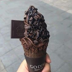 a person holding up an ice cream cone with chocolate toppings on it and a sign that says godiva