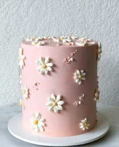 a pink frosted cake with white flowers on the top and bottom, sitting on a plate