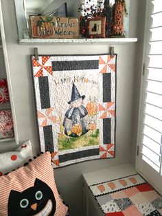 a quilted wall hanging next to a window with a black cat sitting on top of it