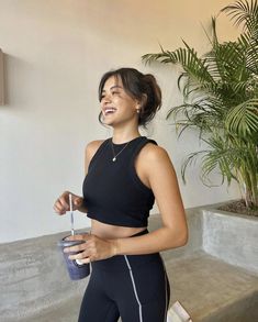 a woman in black sports bra top and leggings holding a water bottle smiling