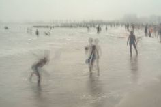 many people are playing in the water at the beach on a foggy, overcast day