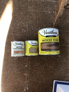 two tins of wood stain sitting on top of a brown floor next to a blue and white sign