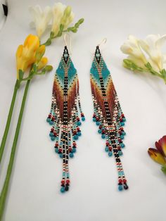 two pairs of colorful beaded earrings sitting on top of a table next to flowers