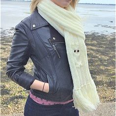 a woman wearing a black leather jacket and white scarf standing in front of the ocean