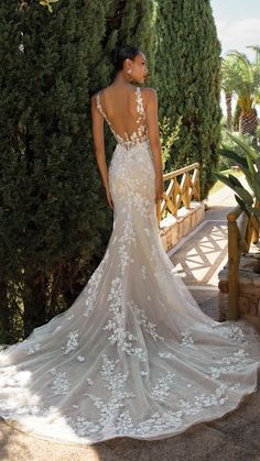 a woman in a wedding dress is standing near some bushes and trees with her back turned to the camera