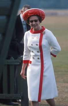 a woman in a white coat and red hat is standing on the grass with other people behind her