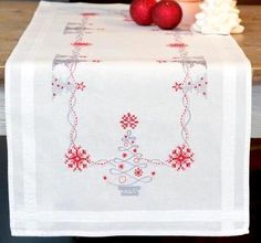 a white table cloth with red flowers on it and candles in the background, along with two christmas balls