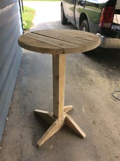 a wooden table sitting in the middle of a driveway next to a parked car,