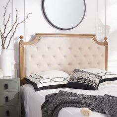 a white bed topped with pillows and a round mirror