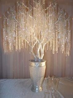 a white vase filled with lots of beads and a tree on top of it in front of a curtain