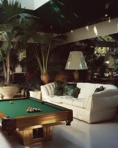 a pool table in the middle of a living room with couches and potted plants