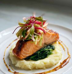 a white plate topped with mashed potatoes covered in greens and salmon on top of it