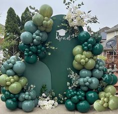 a large green and white balloon arch in front of a house with flowers on it