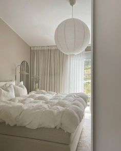 a large white bed sitting in a bedroom next to a window with curtains on it