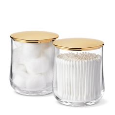 two clear glass jars with gold lids and white cotton balls in the bottom one is empty