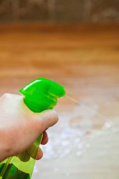 a hand holding a green spray bottle on top of a wooden floor