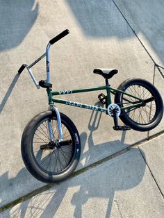 a green bike parked on top of a cement floor next to a person's shadow