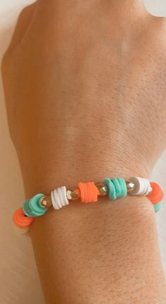 a person's arm with an orange, green and white bracelet on it that has beads