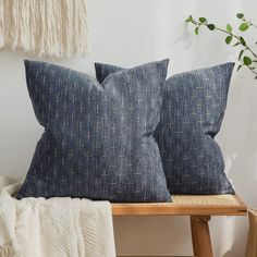 two blue pillows sitting on top of a wooden bench next to a white blanket and potted plant