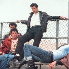 four young men sitting on a bench with one leaning against the fence and another laying down