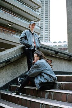 two people are sitting on the stairs in front of a building and one is talking on her cell phone