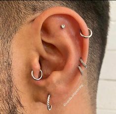 the man is wearing three different ear piercings on his ears and behind his ear