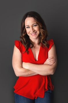 a woman with her arms crossed posing for a photo in front of a gray background