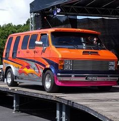 an orange and purple van is parked on the side of a road near a stage