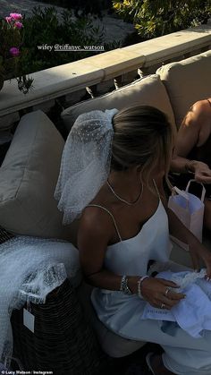 a woman in a wedding dress sitting on a couch with a veil over her head