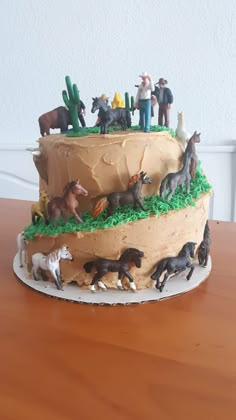 a birthday cake with toy horses and cactus on top is sitting on a wooden table