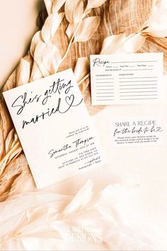 the wedding stationery is laid out next to each other on top of some feathers