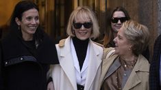 three women standing next to each other in front of a building and one woman wearing sunglasses