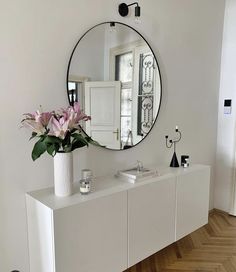 a vase with flowers sitting on top of a white cabinet in front of a mirror