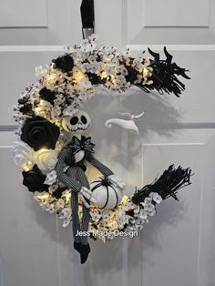 a halloween wreath decorated with black and white flowers, lights and a skeleton on the front door