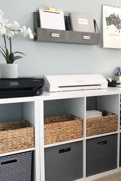 a white shelf with some baskets on top of it next to a printer and other office supplies