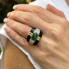 Fabulous emerald, diamond, and onyx cocktail ring handcrafted in 18 karat yellow gold. The band features a bezel set oval cabochon green emerald weighing approximately 4.00 carats, 24 round briliant cut diamonds weighing approximately 2.50 carat total weight, and onyx accent. The diamonds are graded H-I color and SI clarity. The ring measures 19.5mm in width tapering down to 6.5mm, and is currently size 8.5 (can be sized). Weight: 18.4 grams. Luxury Emerald Ring With Oval Cabochon, Luxury Green Cabochons, Luxury Emerald Ring With Oval Cabochon And 17 Jewels, Luxury Oval Cabochon Emerald Ring With 17 Jewels, Luxury Oval Cabochon Emerald Ring, Designer Oval Gemstone Rings, Luxury Emerald Cabochon Ring With Diamonds, Formal Oval Green Enamel Ring, Modern Emerald Cabochon Rings