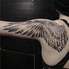 a woman's arm with black and grey wings on her left side, tattoo style