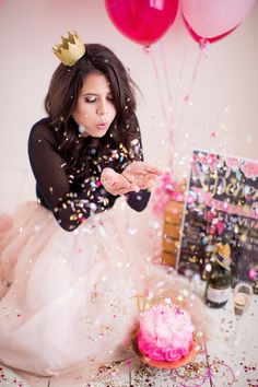 a woman wearing a tiara blowing out confetti on her birthday cake with pink and gold balloons