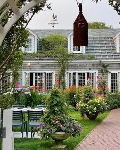 an outdoor dining area in front of a house with potted plants and flowers on the lawn