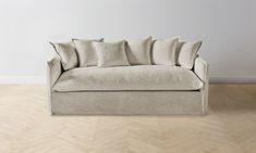 a couch with pillows on it sitting in front of a white wall and wooden floor