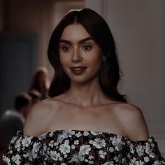 a woman with brown hair wearing a black and white floral print off the shoulder top