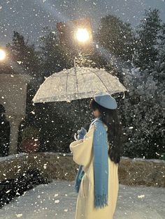 a woman is standing in the snow with an umbrella over her head and lights on behind her