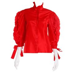 This vintage 1980's Louis Feraud Blouse is in a gorgeous red silk satin and features pretty ruffles and ties. This top has just the right amount of drama with a ruffled collar and red ball buttons down the center front. Each sleeve has three strips of ruffles going from the shoulders to the cuffs, which have pretty ties. This is the kind of blouse that adds depth to a wardrobe and it can be worn with so many separates from jeans to evening skirts! This blouse was originally purchased with a blac Black Ruffled Skirt, Vintage Bodysuit, Edwardian Blouse, Poet Sleeve, Versace Style, Louis Feraud, Evening Skirts, Bodysuit Blouse, Ruffled Blouse