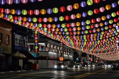 many colorful lights hanging from the ceiling above a street with cars driving down it at night