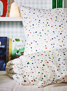 a bed topped with pillows and blankets next to a book shelf filled with children's books