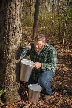 a man squatting next to a tree and holding two buckets in his hands