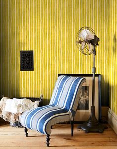 a striped chair in front of a yellow wall with a fan on top of it