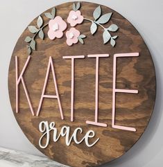 a wooden sign that says kate grace with flowers and leaves on the front in pink