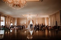 a couple getting married in front of an elegant wedding ceremony room with chandelier