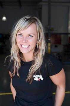 a woman with blonde hair and blue eyes smiles at the camera while wearing a black t - shirt